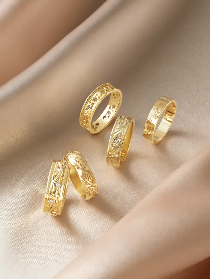 Multiple gold wedding bands with engraved designed around the ring on beige fabric surface