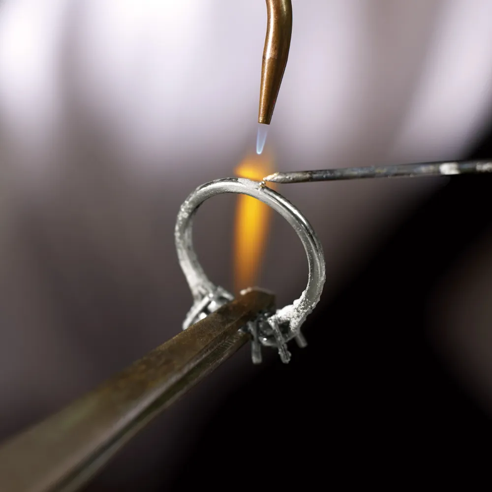 Jeweler soldering a ring with a flame, showcasing craftsmanship at Virtus Collective, Irvine's fine jewelry store.