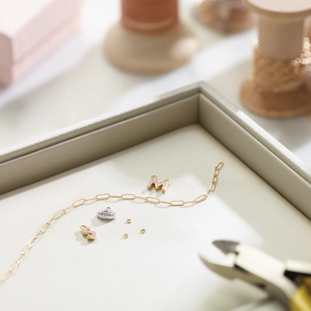 Gold chain with charms next to it about to be put together with tools