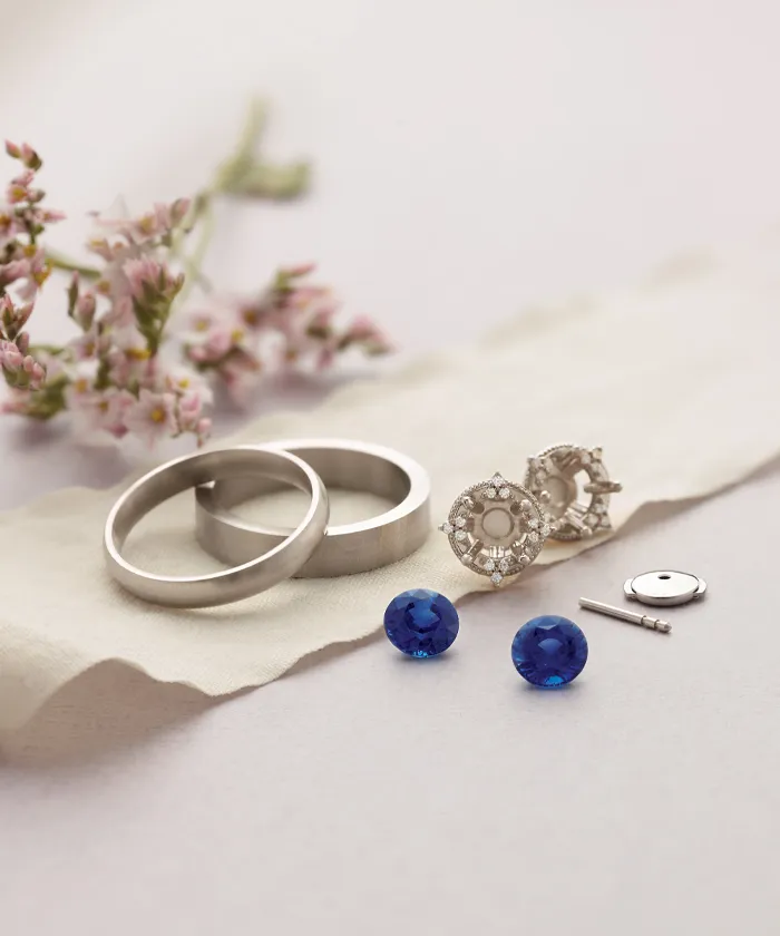 Dismantled ring with blue gemstones laying next to pink flowers on a surface