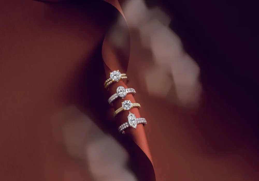 Four engagement rings with various diamond shapes slipped through a brown ribbon