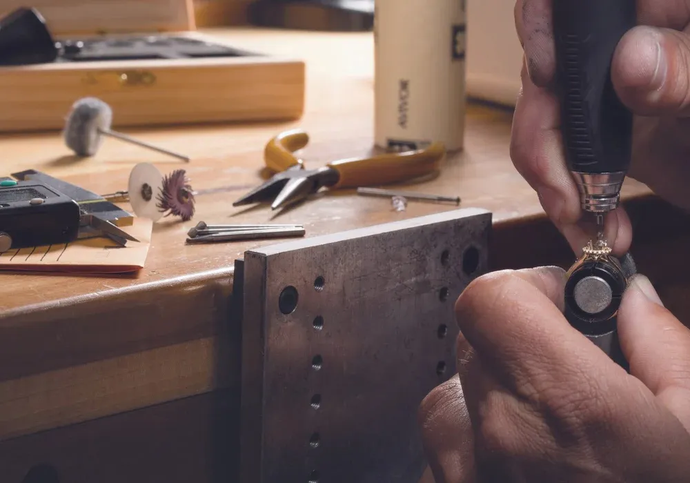 Person repairing a ring prong with a tool at a work bench