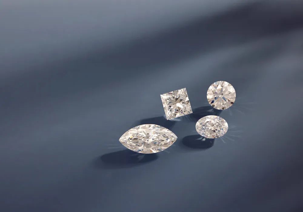 Four diamonds with shapes including marquise, oval, round, and square laying on blue background