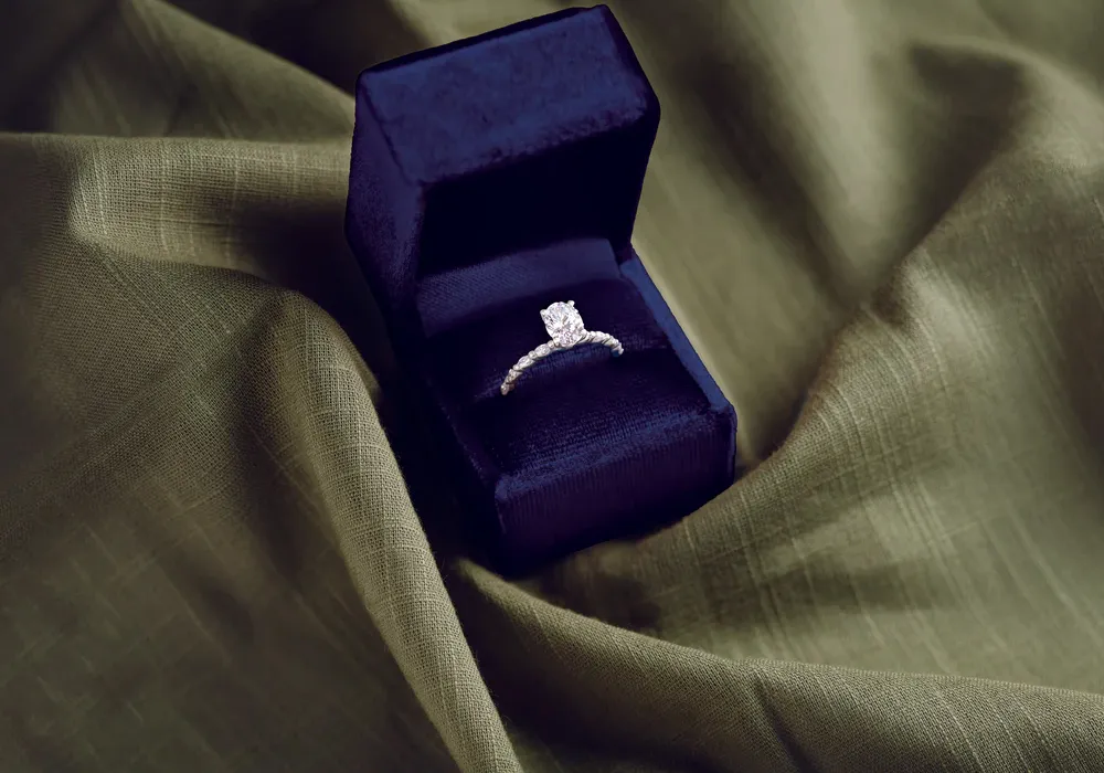 Oval diamond engagement ring sitting in dark blue ring box on green fabric background