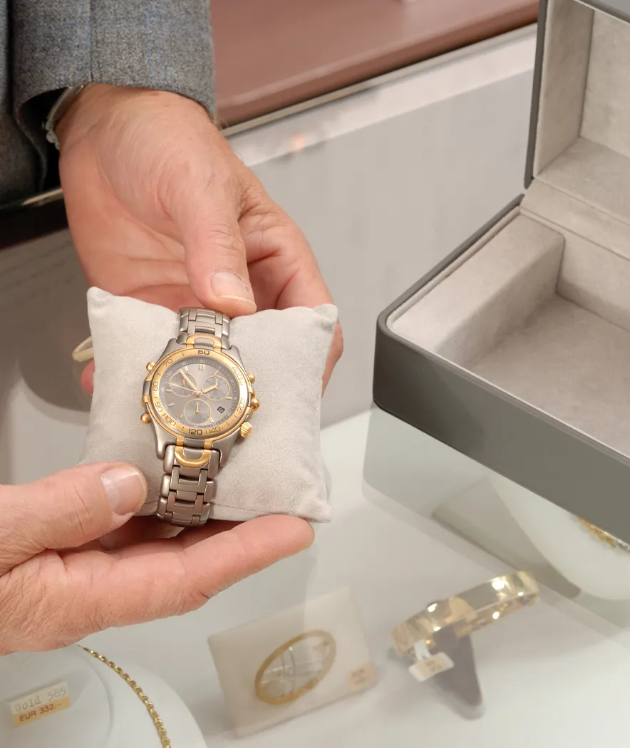 Man presenting a watch laying on a small plush pillow on top of a jewelry case seen in a jewelry store