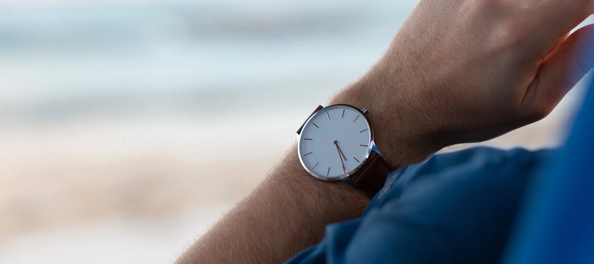 Man wearing watch with brown leather band on a sandy beach