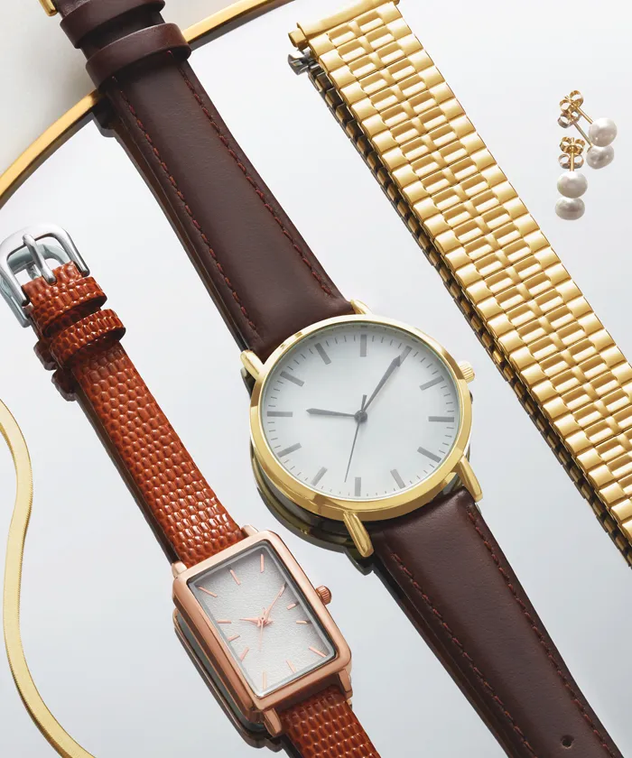 Rectangular and circular watch laying next to one another on reflective surface with a gold watch band next to them