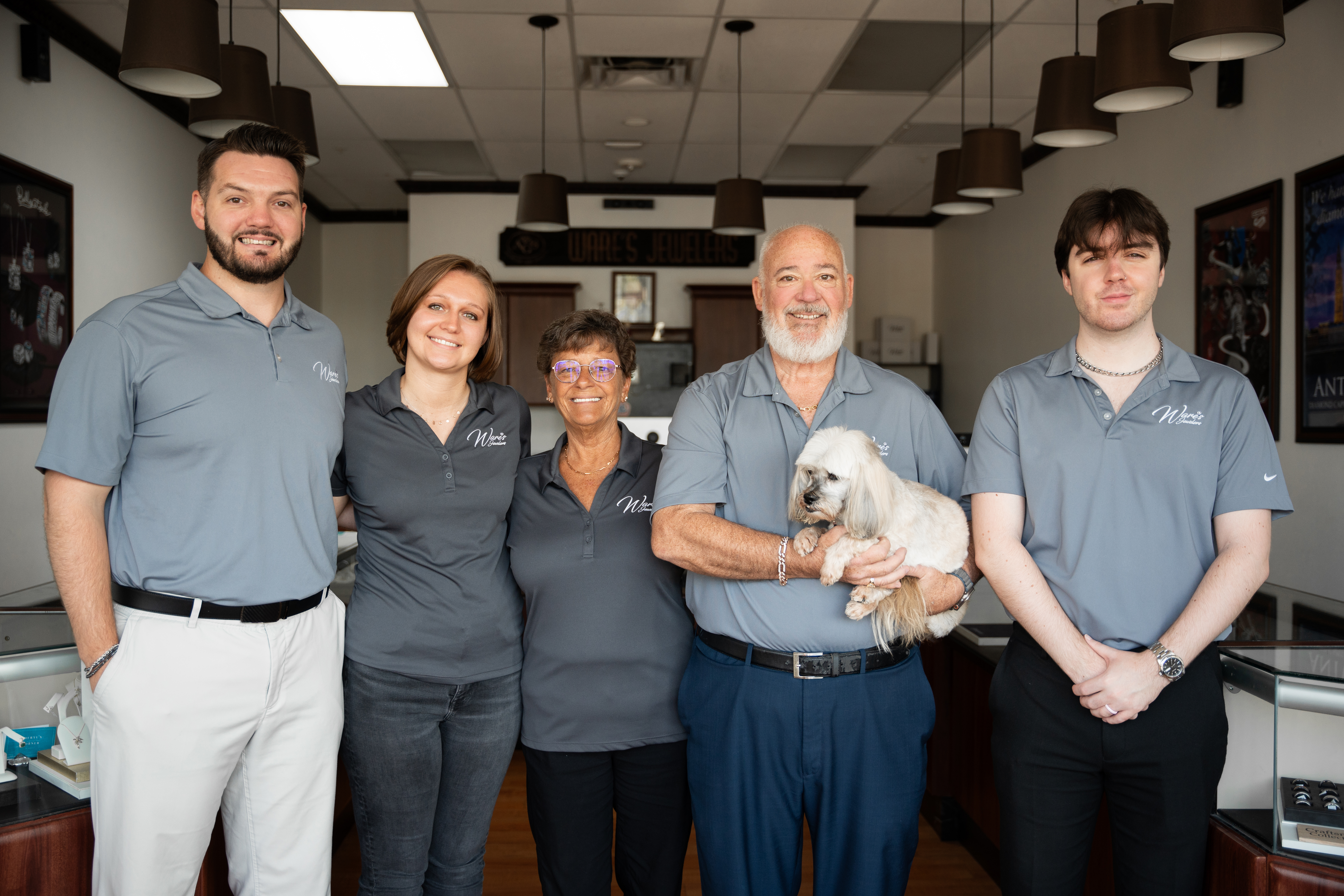 The team at Ware's Jewelers in Bradenton, smiling together with a small dog in a jewelry store setting.
