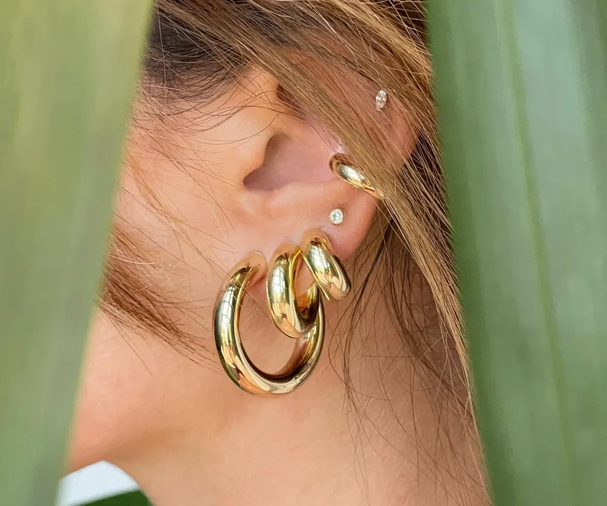 Close-up of an ear with multiple gold hoop earrings and small diamond studs.