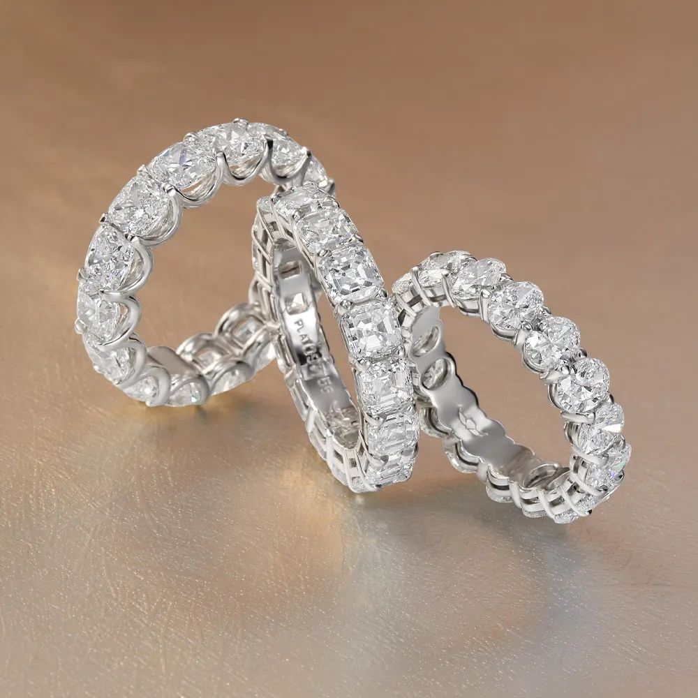 Three diamond eternity bands on a gold surface, showcasing intricate settings and sparkling stones.