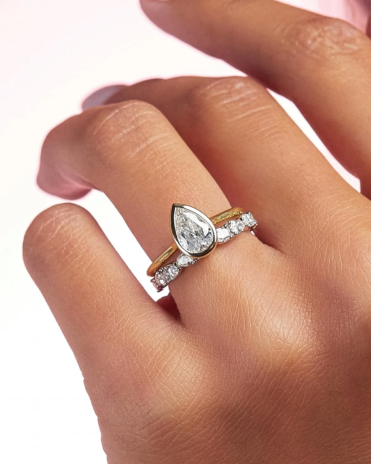Pear-shaped diamond ring with gold band on hand.