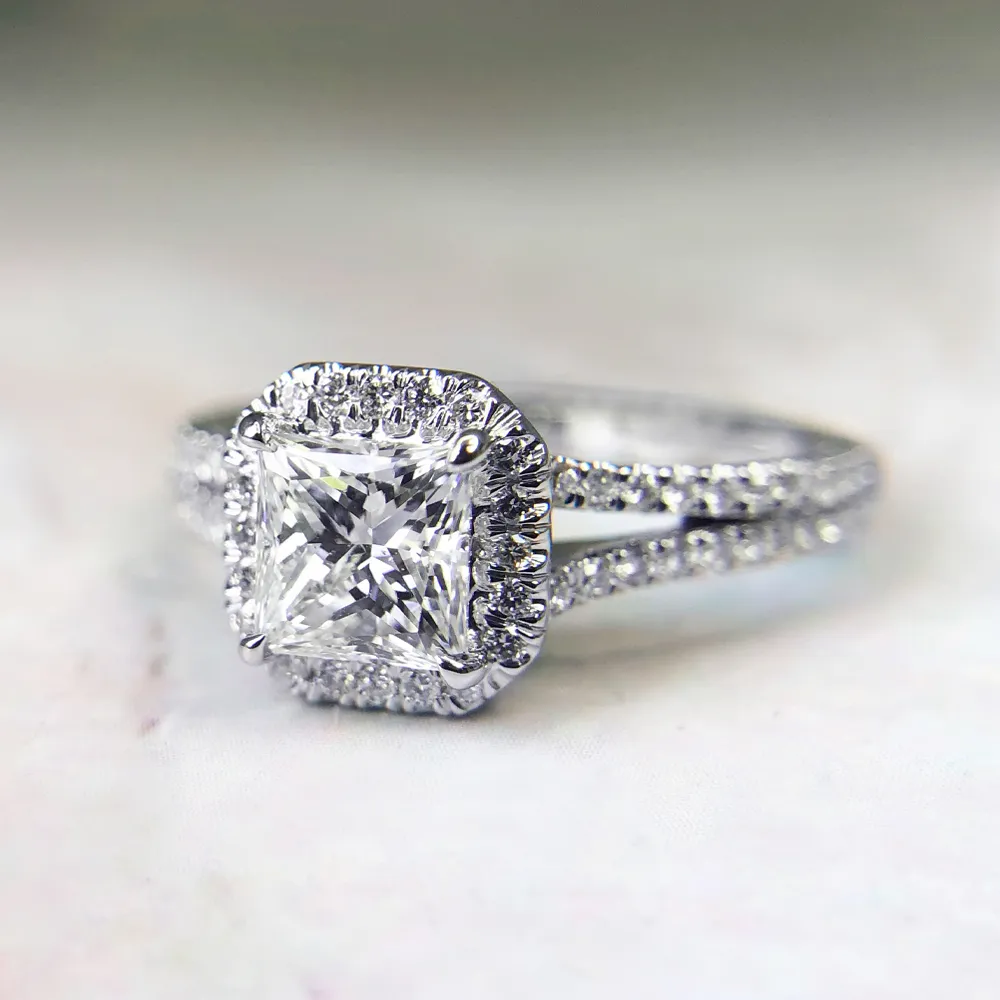 Elegant engagement ring with a square-cut diamond and halo setting on a split shank band.
