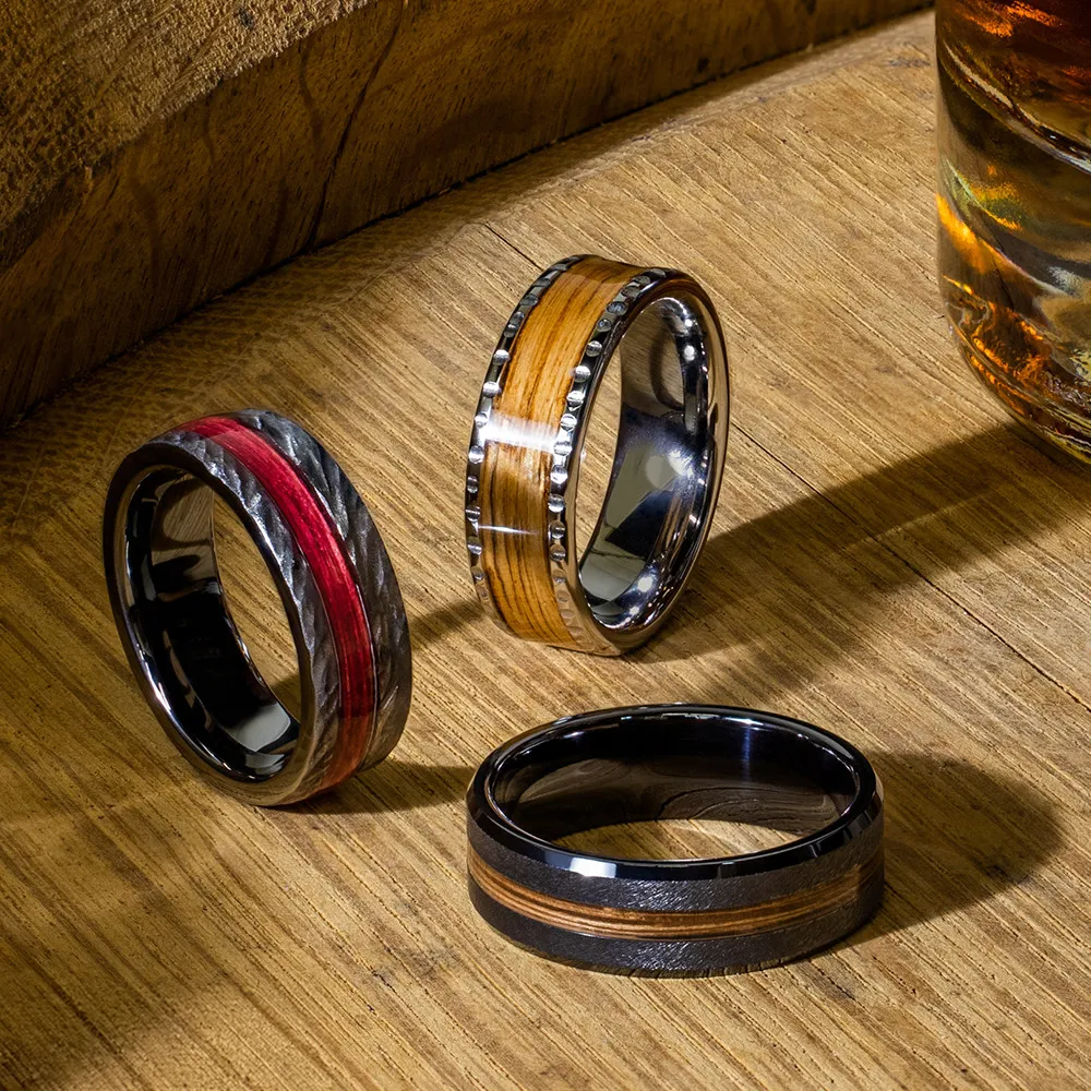 Men's wedding bands with wood and metal inlays on a wooden surface.