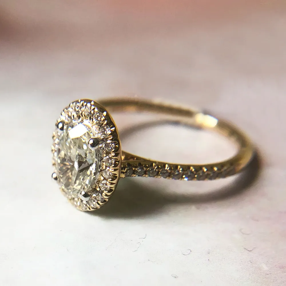 A gold engagement ring with an oval diamond and halo setting on a light background.