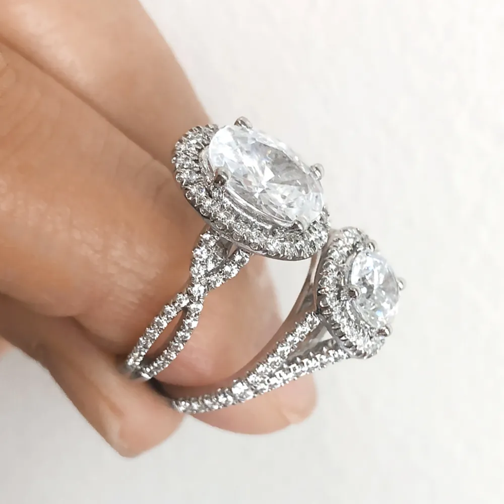 Two diamond rings with oval stones and halo settings on a person's fingers.