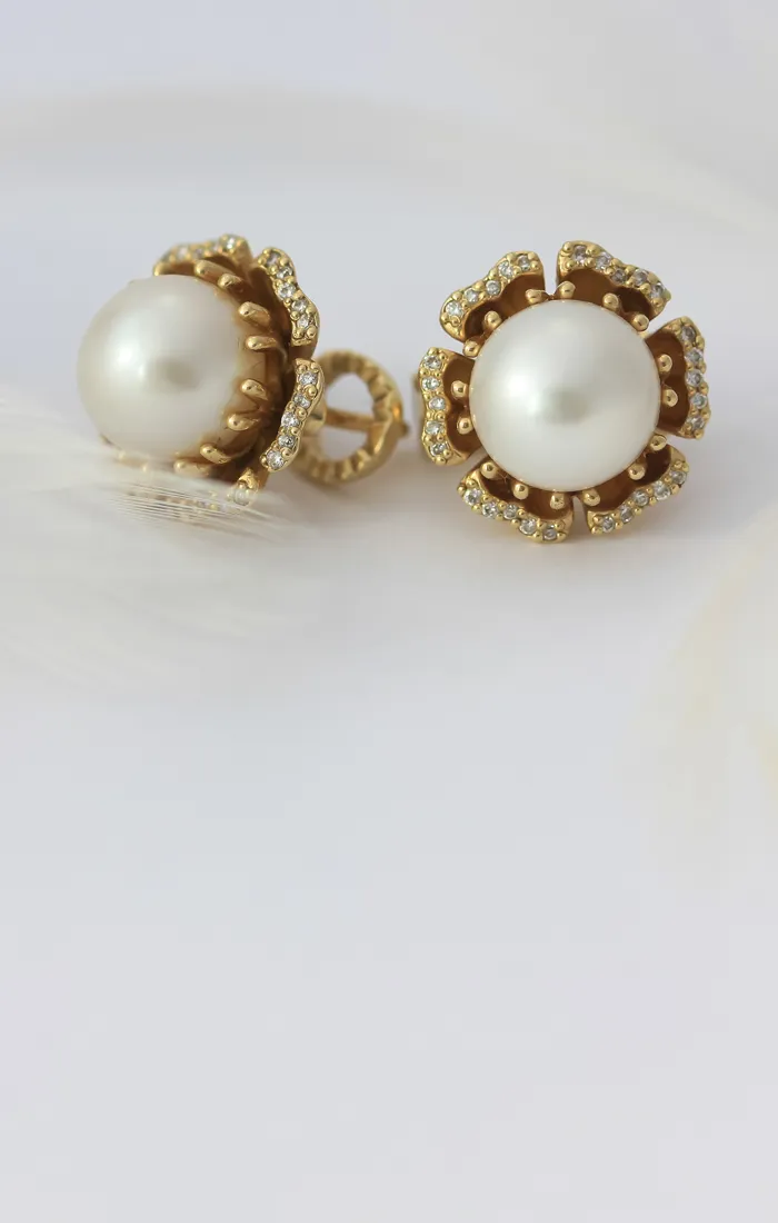 Gold and pearl earrings with diamond accents on a white feather background.