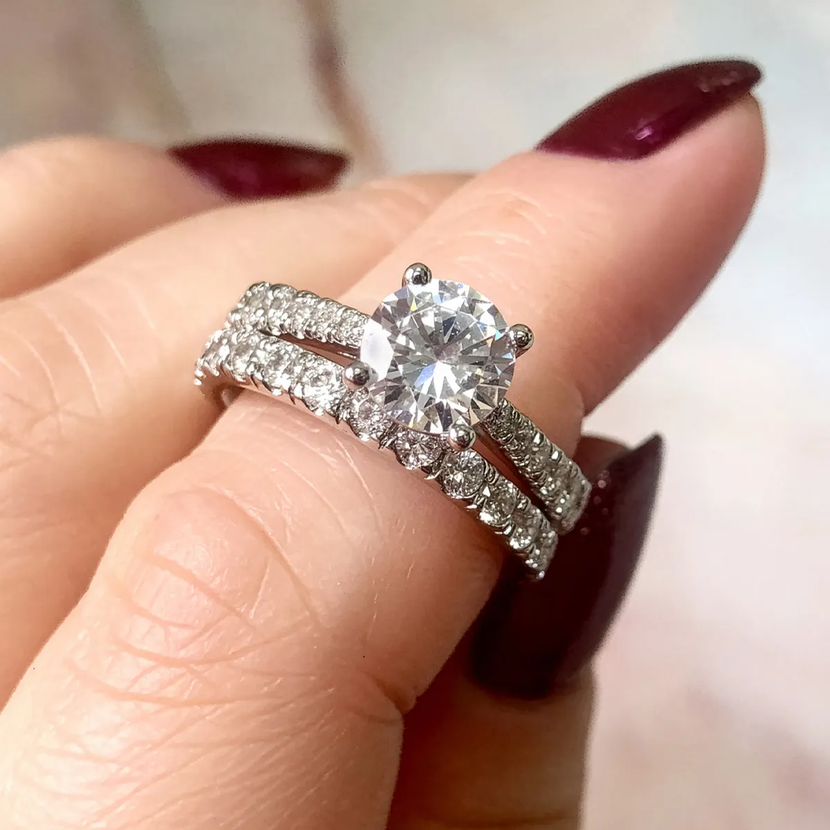 Diamond engagement ring with matching band held between fingers.