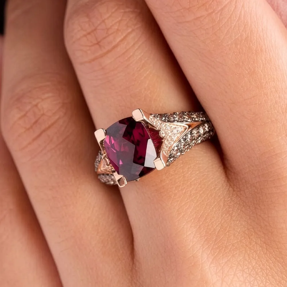 A hand wearing a ring with a large red gemstone and diamond accents.