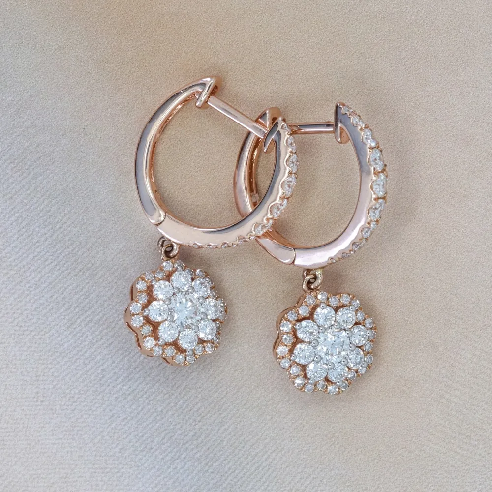 Elegant rose gold hoop earrings with diamond floral pendants on a beige background.