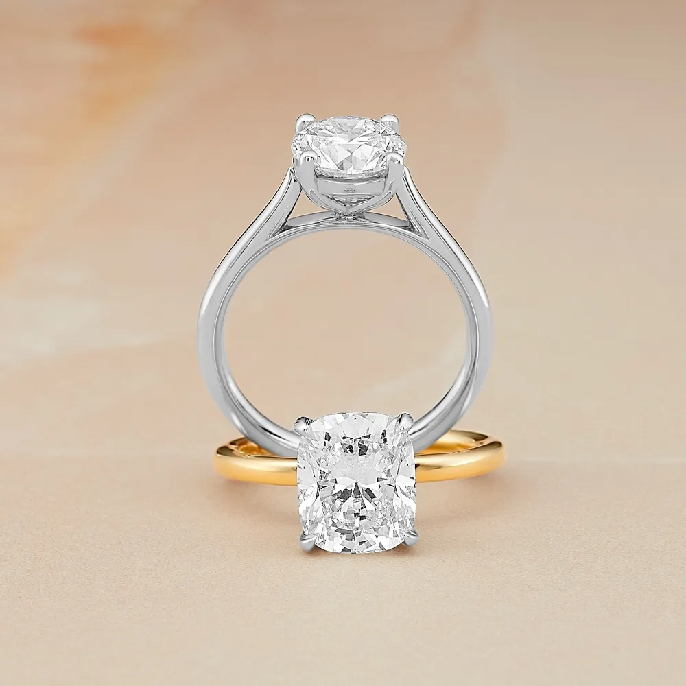 Two diamond rings, one with a round cut on a silver band, and another with a cushion cut on a gold band, displayed elegantly.