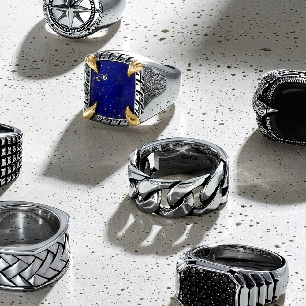 Men's rings with various designs on a textured surface.