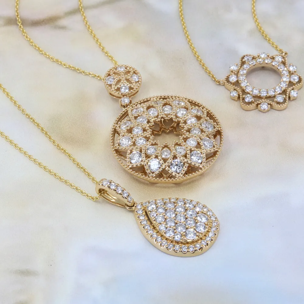 Three gold necklaces with intricate diamond-studded pendants on a light background.