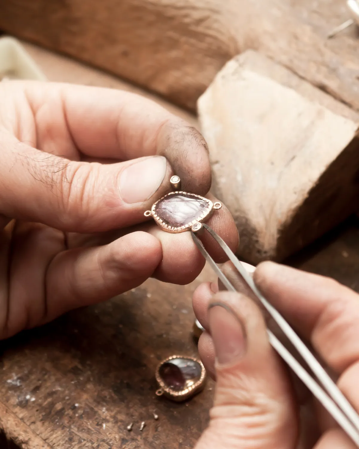 Jeweler's hands working on a gemstone setting with tweezers.