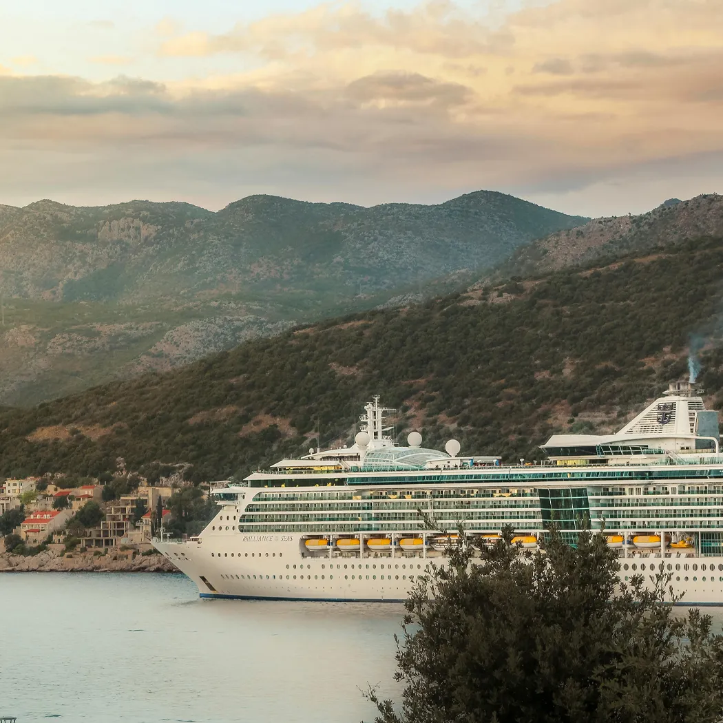 Cruise ship anchored near mountains at sunset, showcasing a scenic coastal view.