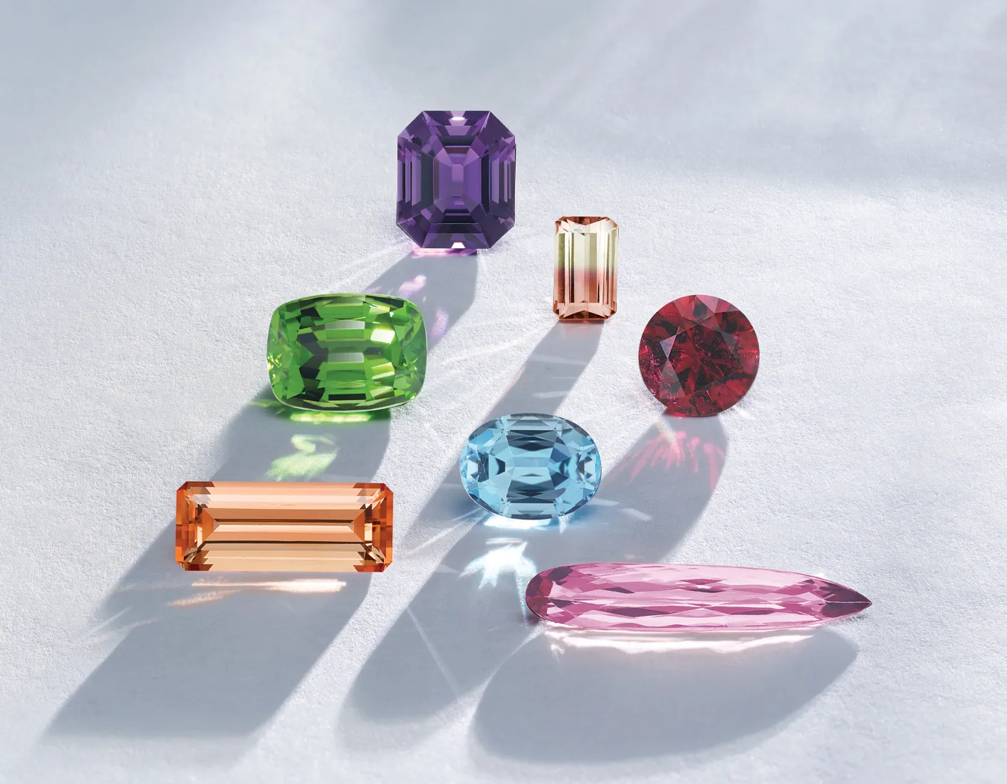 A variety of colorful gemstones on a light surface, casting shadows.
