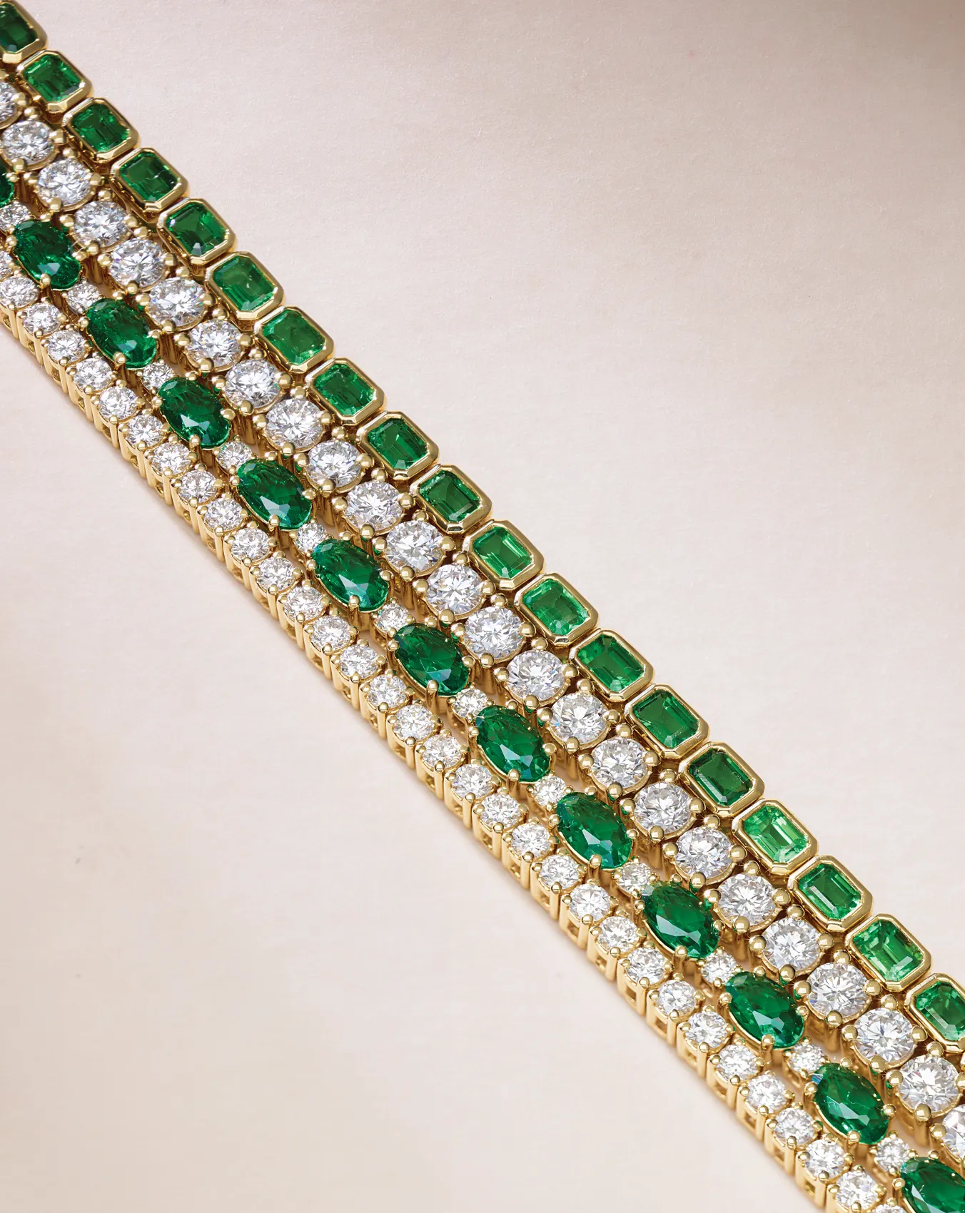 Elegant gold bracelet with green emeralds and white diamonds in a row pattern.