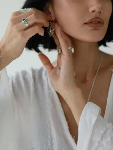 Woman adjusting earring, wearing rings and white blouse. Explore Mother's Day gifts under $500 at Whidby Jewelers.
