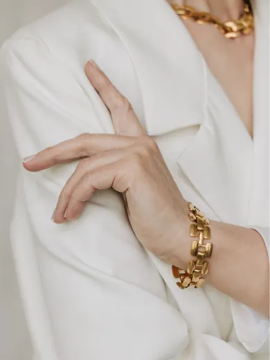 Elegant gold bracelet and necklace on person in white blazer. Explore Mother's Day gifts under $750.
