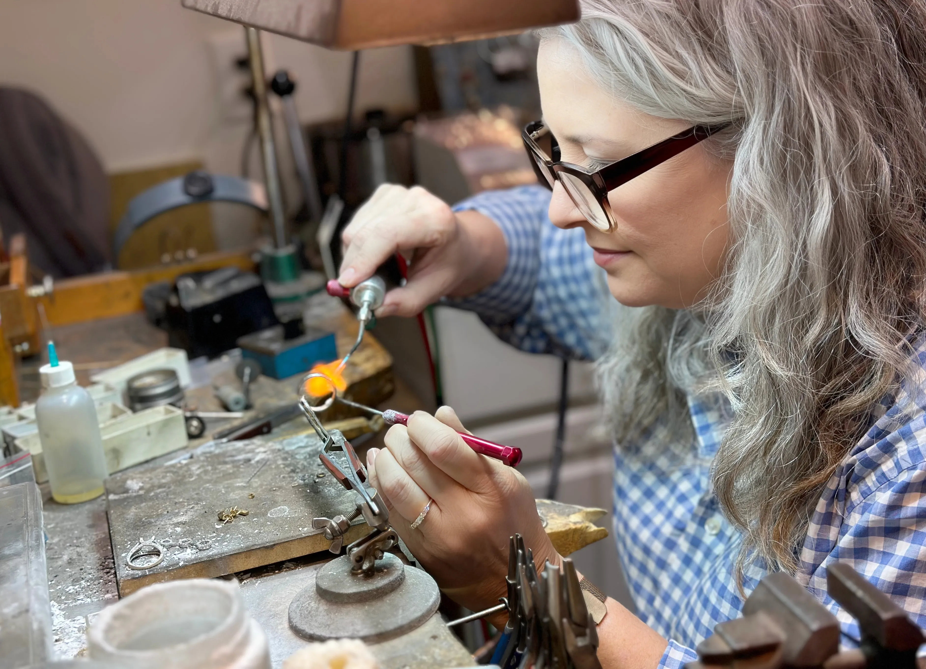 Jeweler working on a piece with a torch in a workshop, showcasing craftsmanship at Whidby Jewelers in Madison.