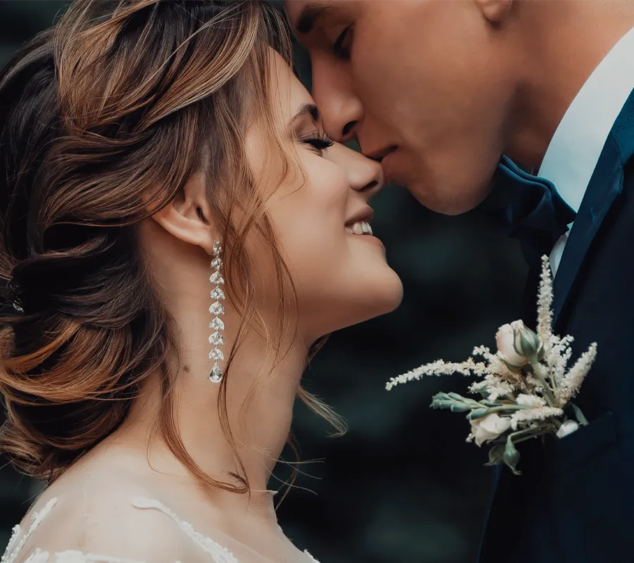 Bride and groom sharing a tender moment, foreheads touching, with the bride holding a floral bouquet. Shop engagement now!