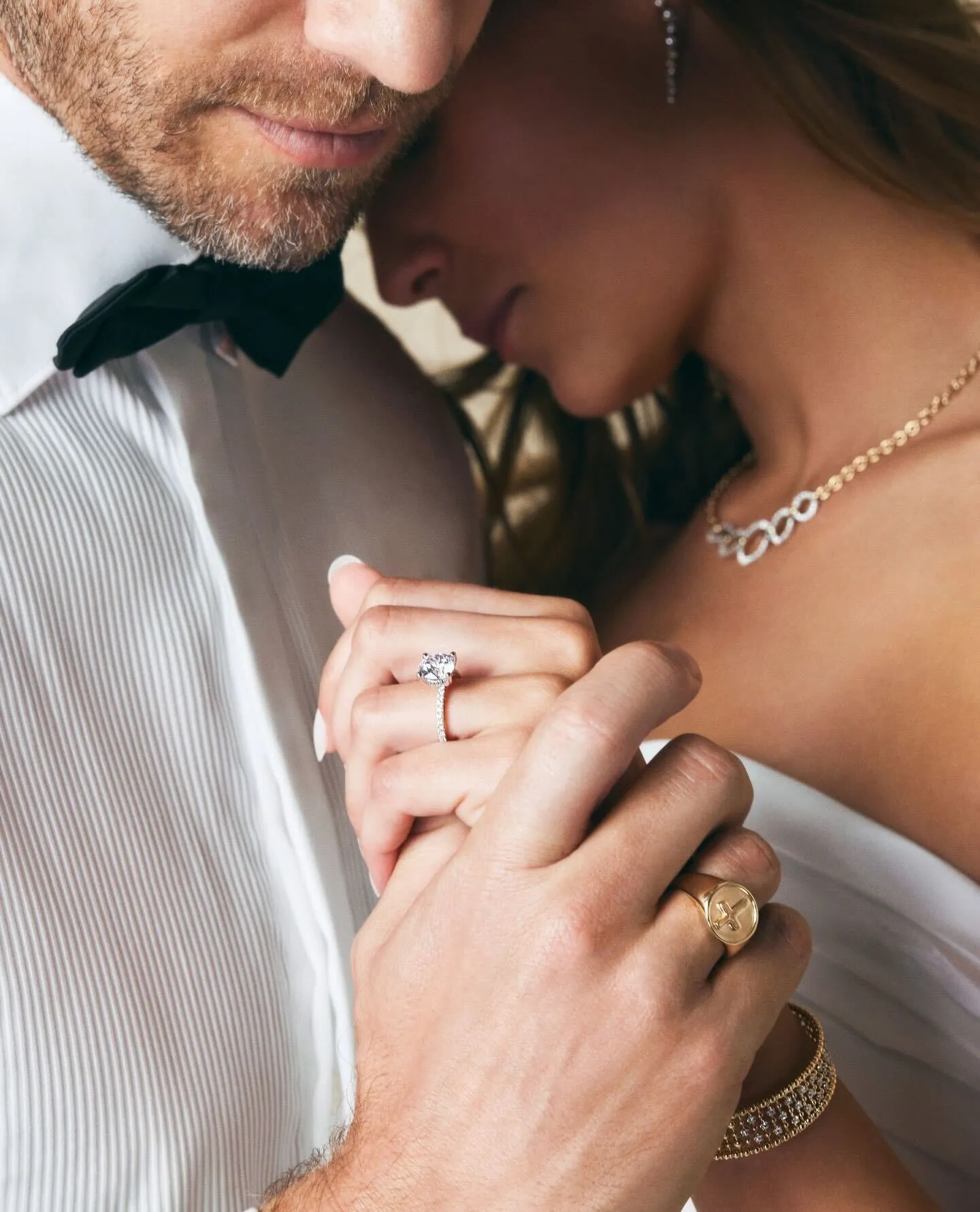 A couple holding hands, showcasing an engagement ring and jewelry.