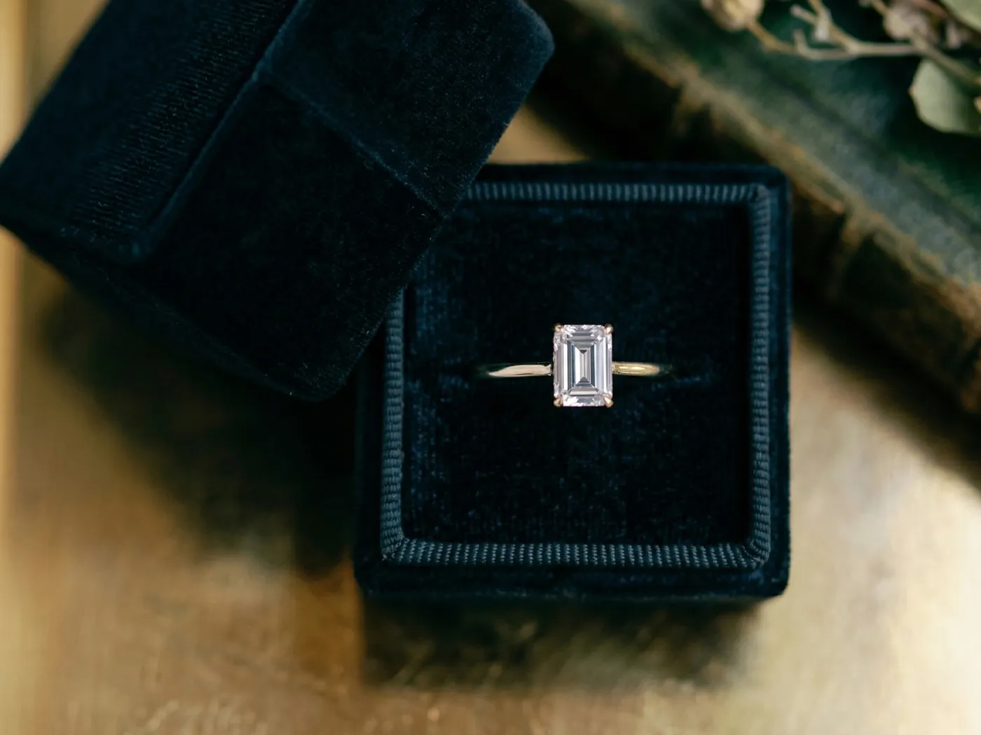 Emerald-cut diamond ring in a black velvet box on a wooden surface.