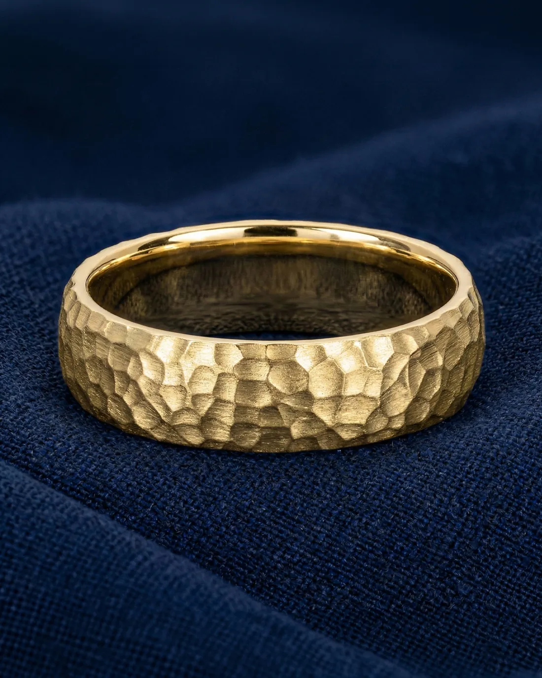 Hammered gold ring on dark blue fabric. Shop men's bands at Wise Family Quality Jewelers.