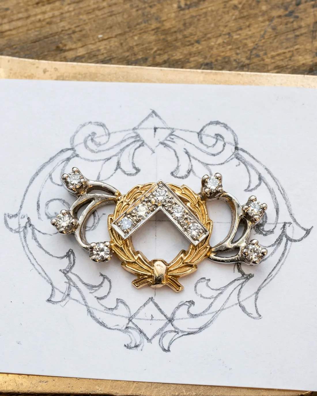 A gold and silver diamond brooch on a decorative sketch background.