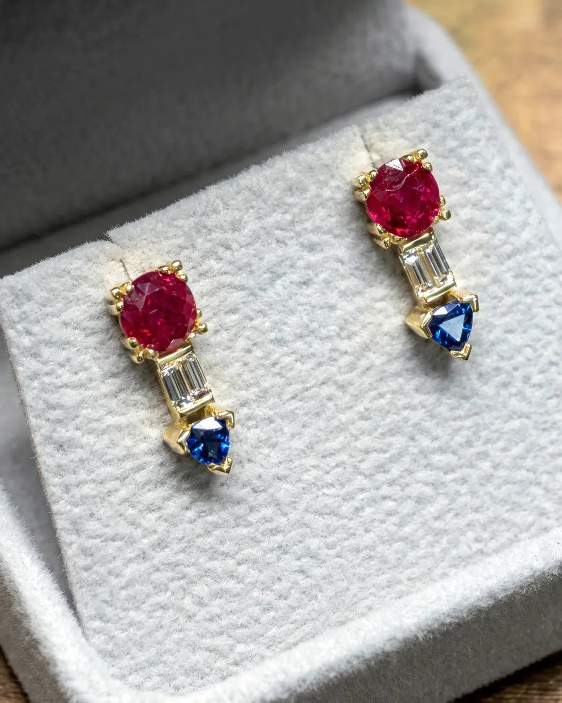 Gold earrings with red, blue, and clear gemstones in a jewelry box.