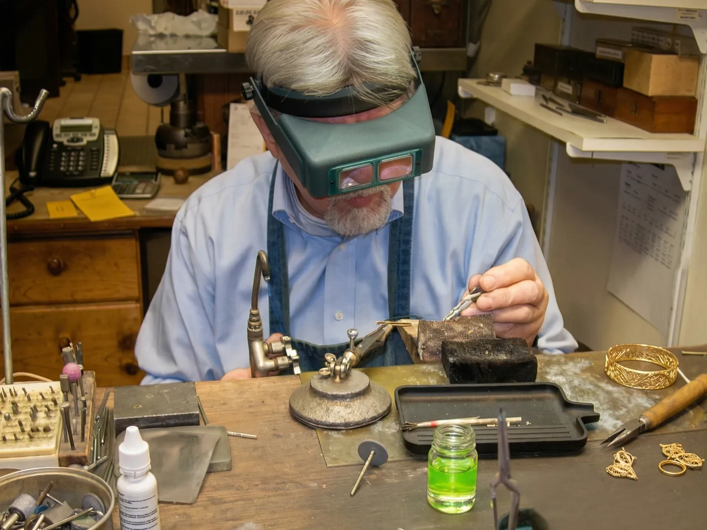 Jeweler working at a bench with magnifying glasses and tools.