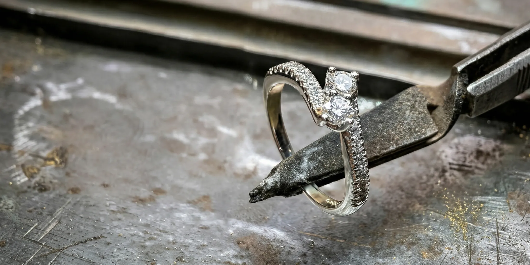 A diamond ring held by pliers on a workbench, showcasing craftsmanship.