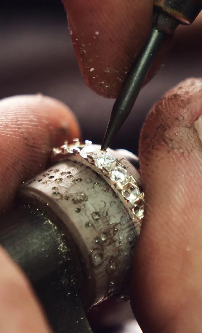 Jeweler setting diamonds on a ring with a tool, showcasing craftsmanship.