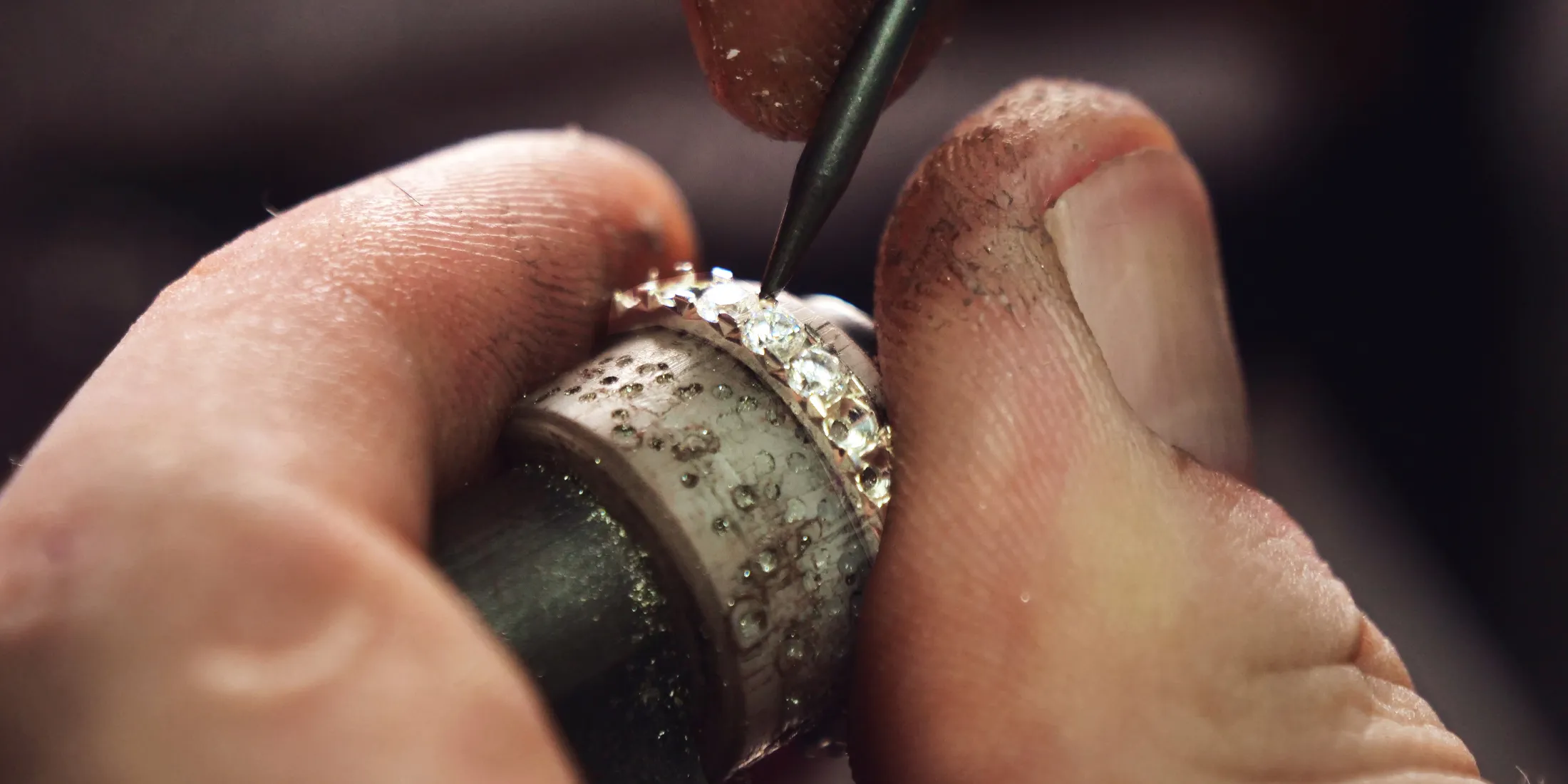 Jeweler setting diamonds on a ring with a tool, showcasing craftsmanship.