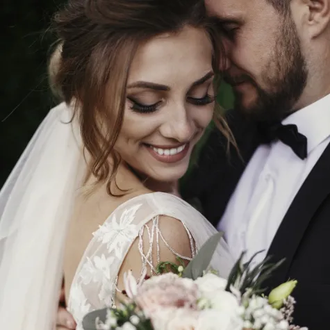 Happy bride wearing ivory veil and wedding dress hugging her husband wearing a black suit, white dress shirt and black bow tie