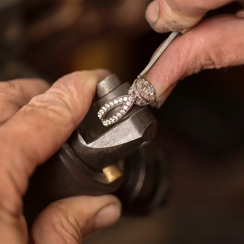 Jeweler working on a diamond ring with a tool in hand.