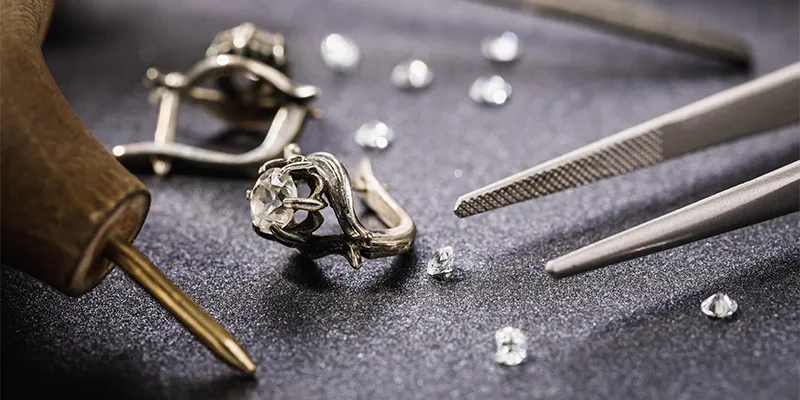 Jewelry tools, diamond ring, and loose diamonds on a dark surface.