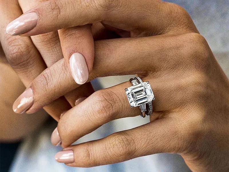 Close-up of a woman's hand with diamond ring and earrings, showcasing fine jewelry.