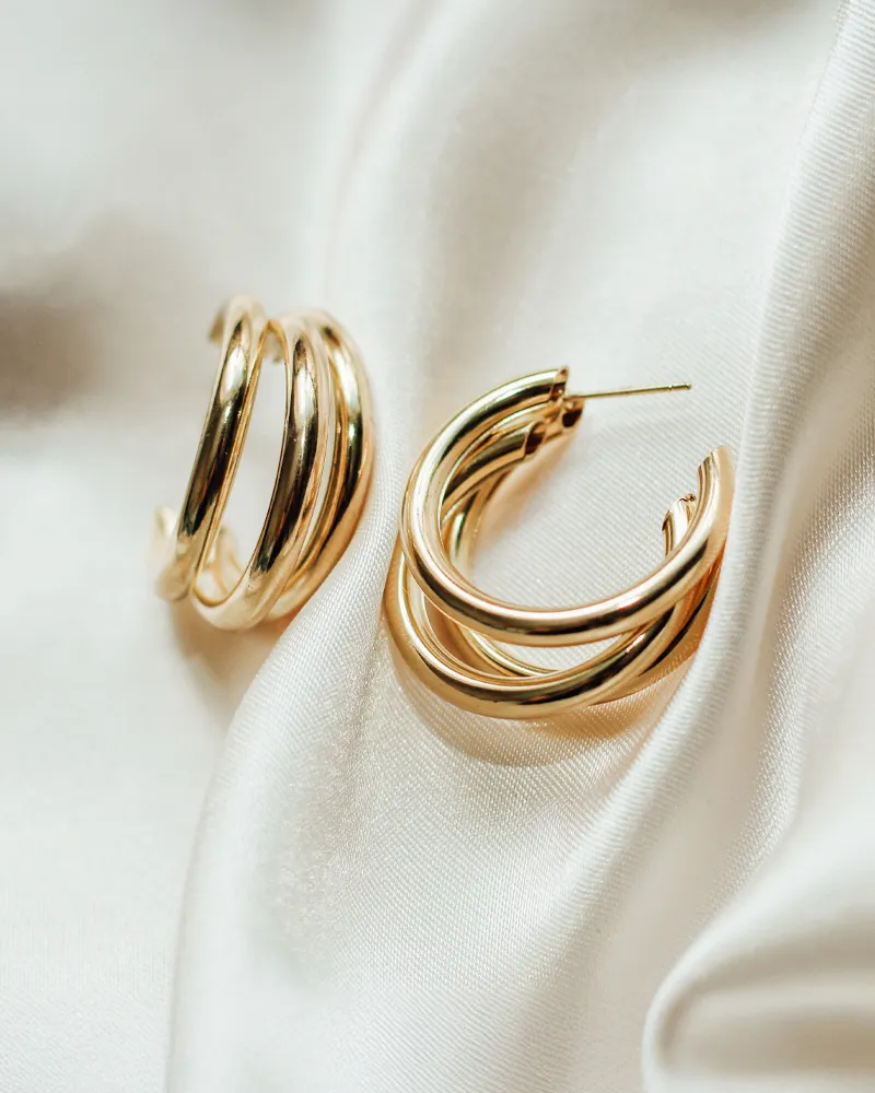 Gold hoop earrings on white satin fabric.