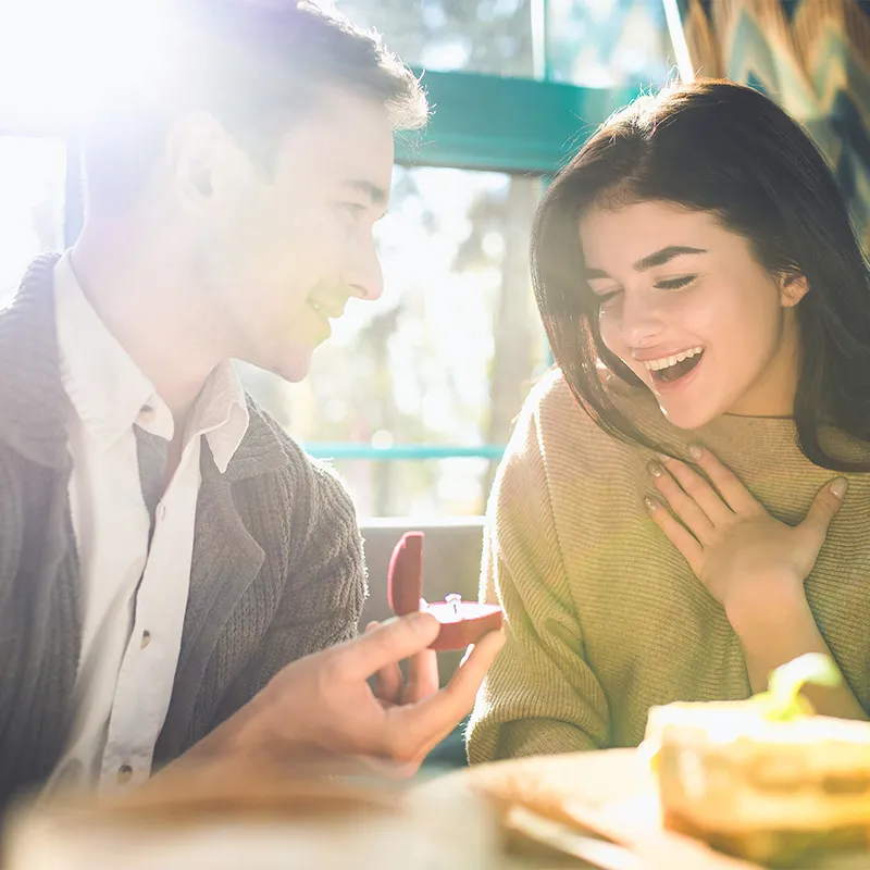 A couple shares a joyful moment as the man proposes with a ring in a cozy setting.