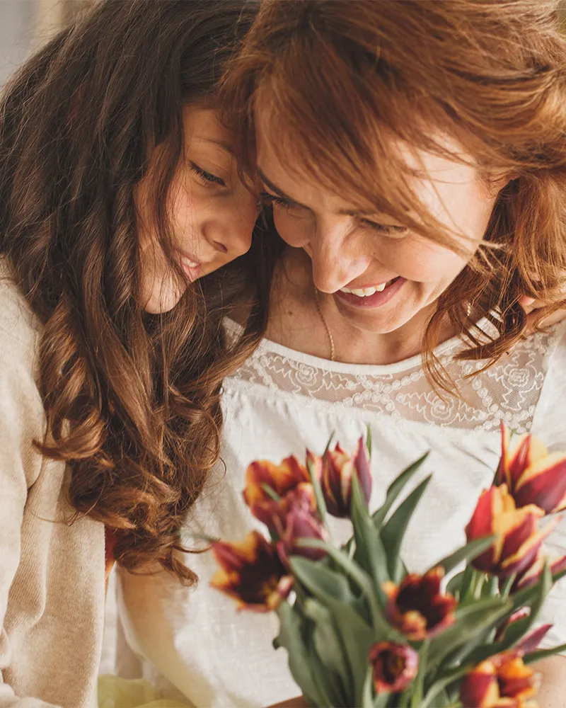 A mother and daughter smiling and embracing with a bouquet of tulips.